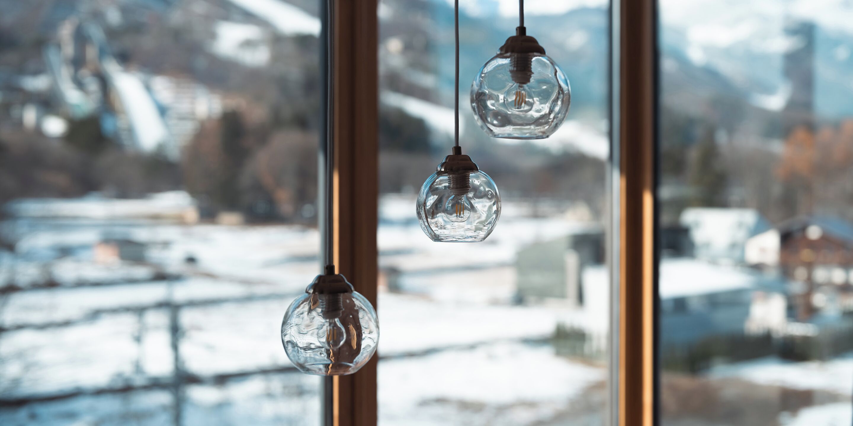 Three hanging glass globes in a window with a snowy landscape view.