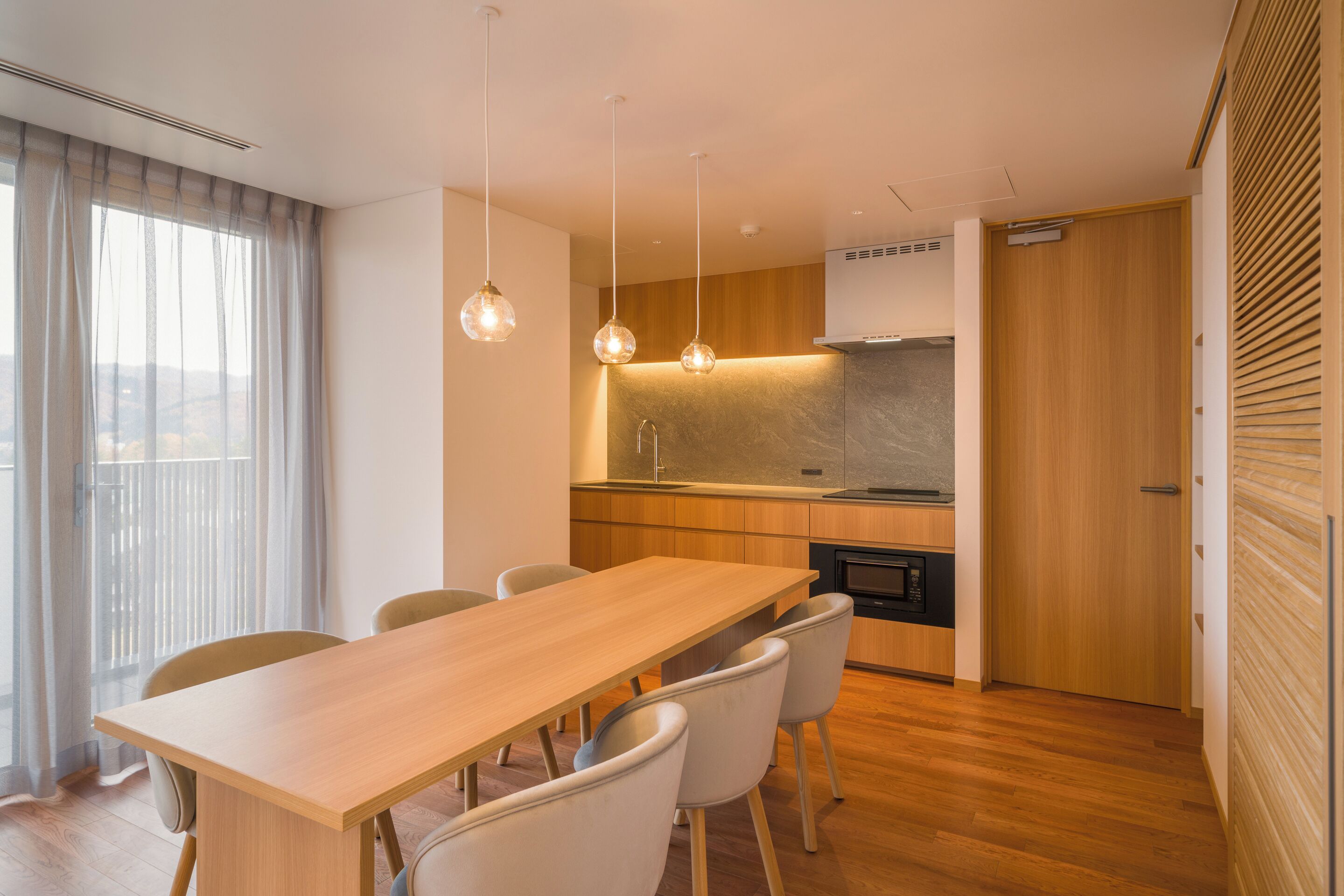 Una cocina moderna con armarios de madera, una campana extractora de acero inoxidable y una zona de comedor con mesa y sillas de madera.
