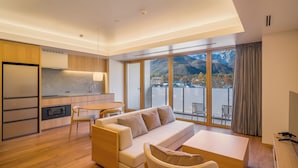 A modern living room with a sofa, chairs, a coffee table, a TV, and a balcony with a mountain view. - HOTEL LA VIGNE HAKUBA by Onko Chishin (Hakuba)