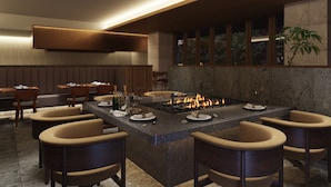 A modern restaurant with a central island featuring a built-in fire feature, surrounded by cushioned chairs. - HOTEL LA VIGNE HAKUBA by Onko Chishin (Hakuba)