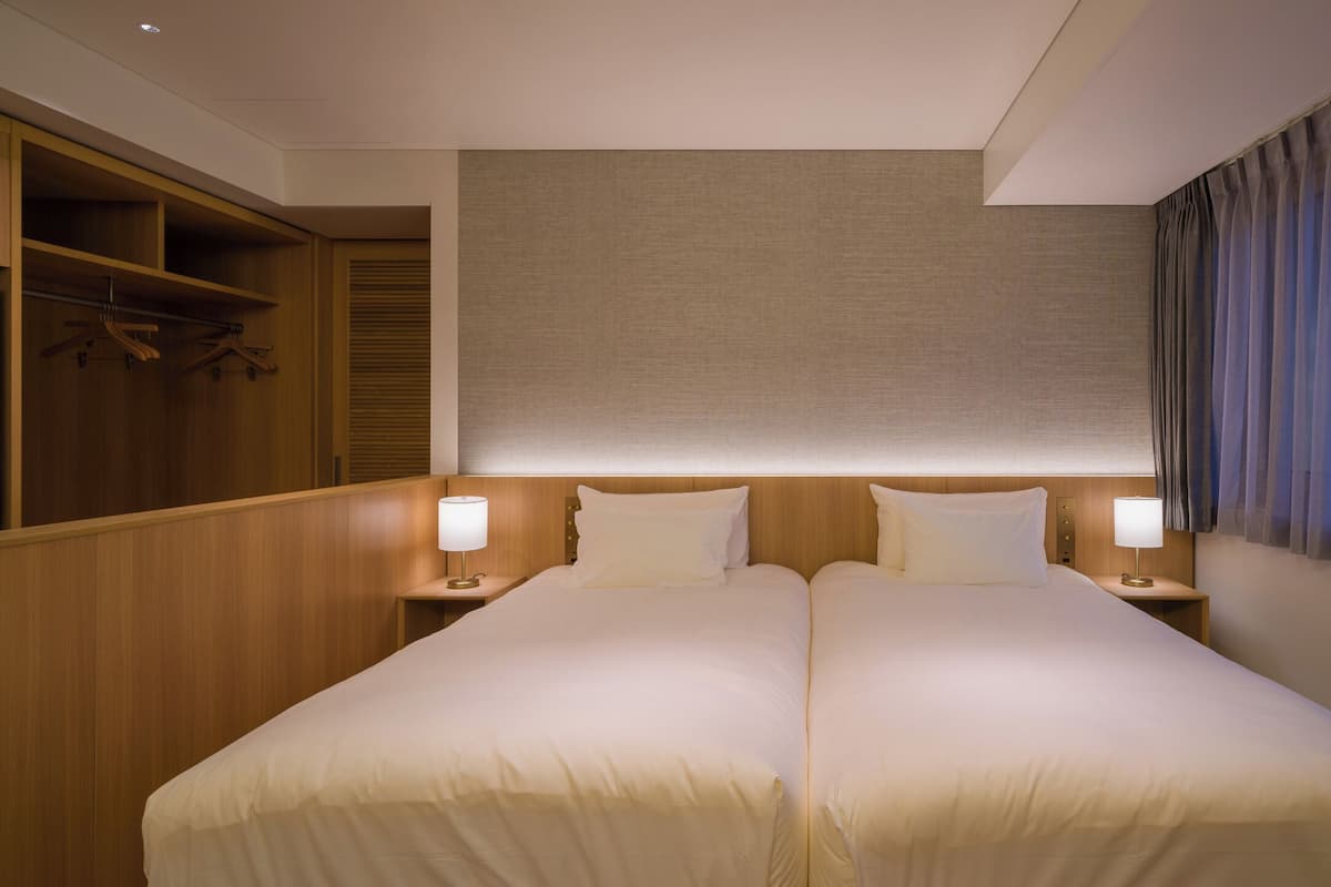 A hotel room with two beds, a walk-in closet, and a large window with curtains.