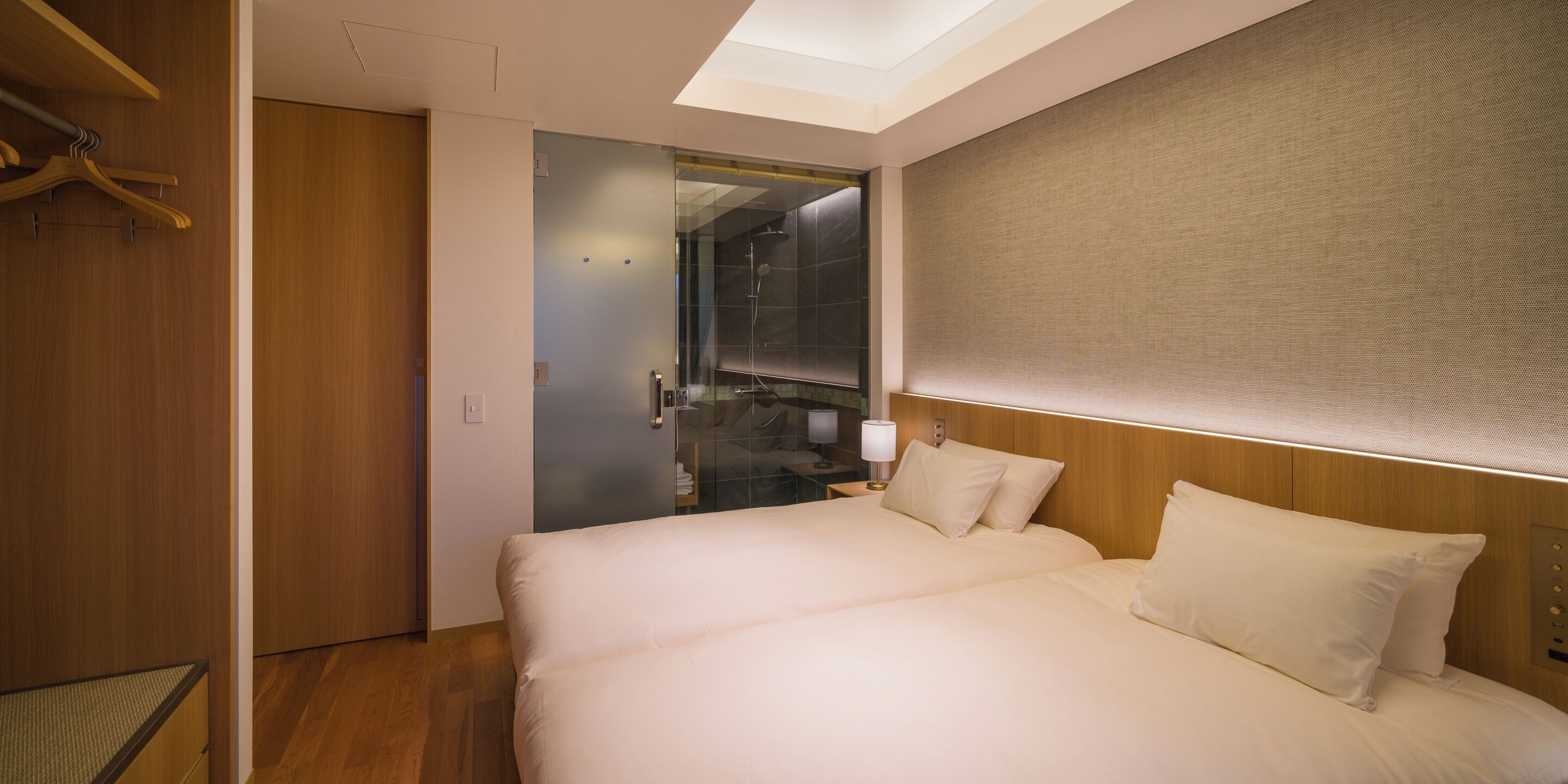 A hotel room with a large bed, a wooden wardrobe, and a glass shower enclosure.
