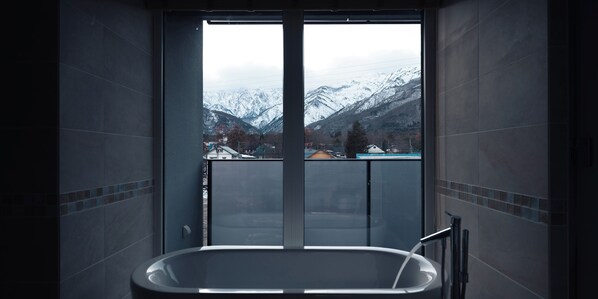 Un baño con bañera y vistas a montañas nevadas a través de un ventanal grande.
