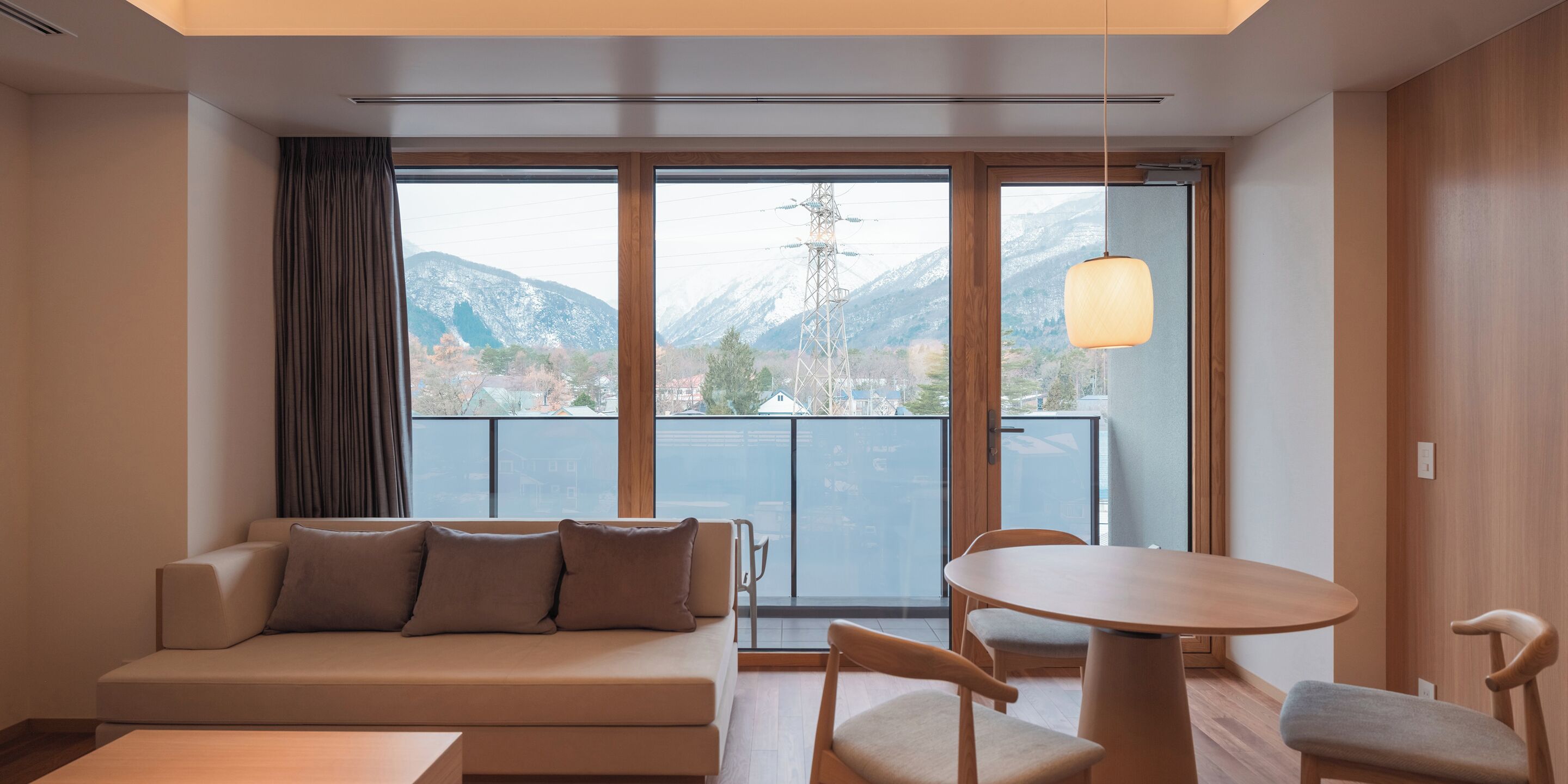A modern hotel room with a sofa, chairs, a table, and a balcony with a mountain view.
