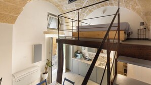 Quarto compacto, com vários níveis, incluindo cama em mezanino, pequena cozinha e escada.