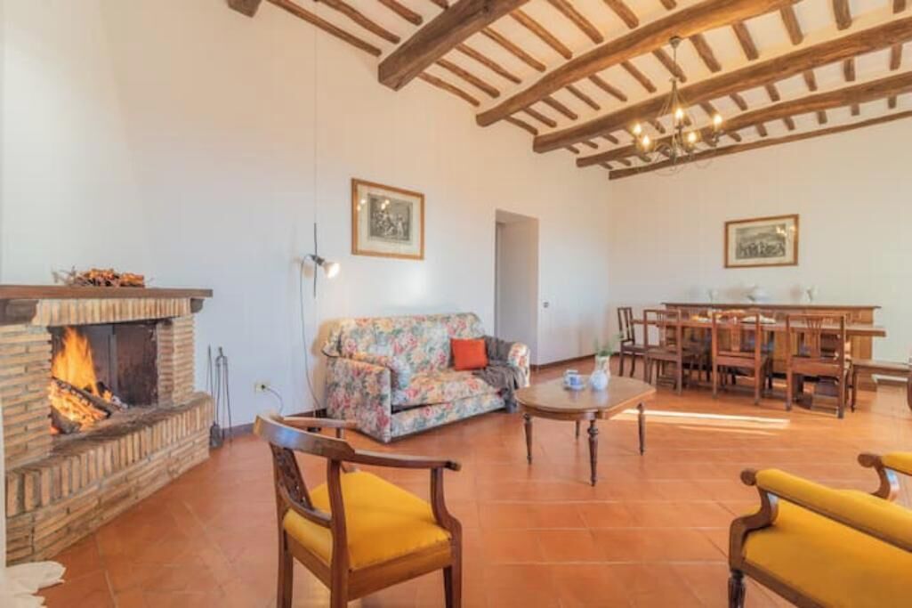 A cozy living room with a fireplace, a floral sofa, wooden furniture, and a dining area.