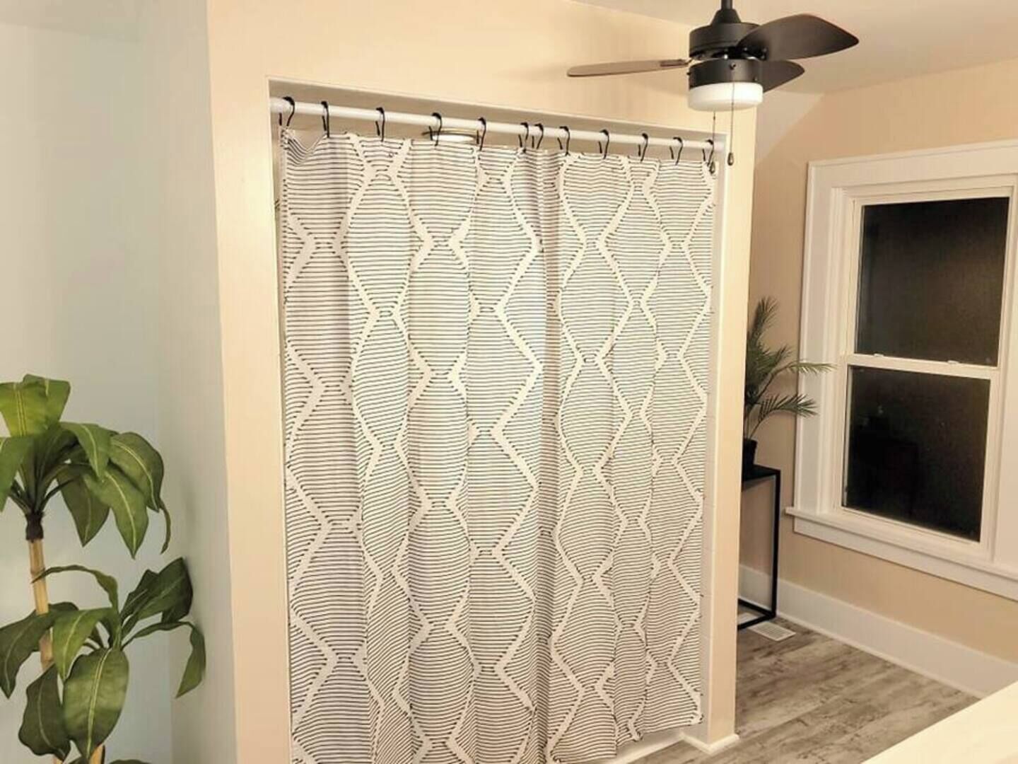 A bathroom with a shower curtain featuring a geometric pattern, a ceiling fan, a potted plant, and a window with blinds.