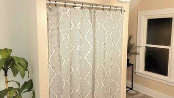 A bathroom with a shower curtain featuring a geometric pattern, a ceiling fan, a potted plant, and a window with blinds.