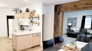 A modern kitchen with a central island, a dining area with a black table, and a living room with a sofa and a coffee table.