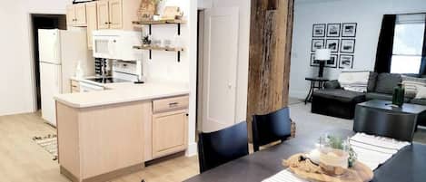 Una cocina moderna con una isla central, una zona de comedor con una mesa negra y una sala de estar con sofá y mesa de centro.