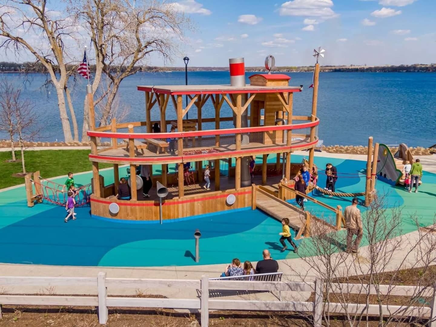 A wooden play structure with a lookout tower and slides, surrounded by a blue pool.
