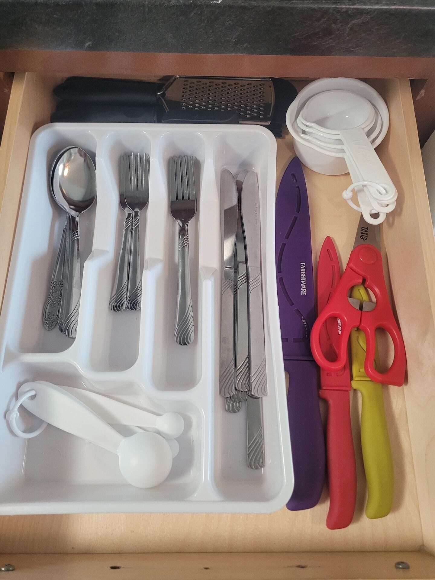 Un cajón con cubiertos, un cuchillo, un par de tijeras y un rallador.