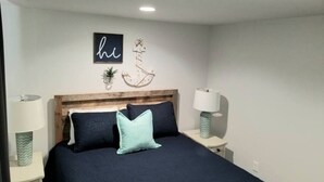 A bedroom with a bed, two bedside tables, a wall-mounted light fixture, and decorative wall art.