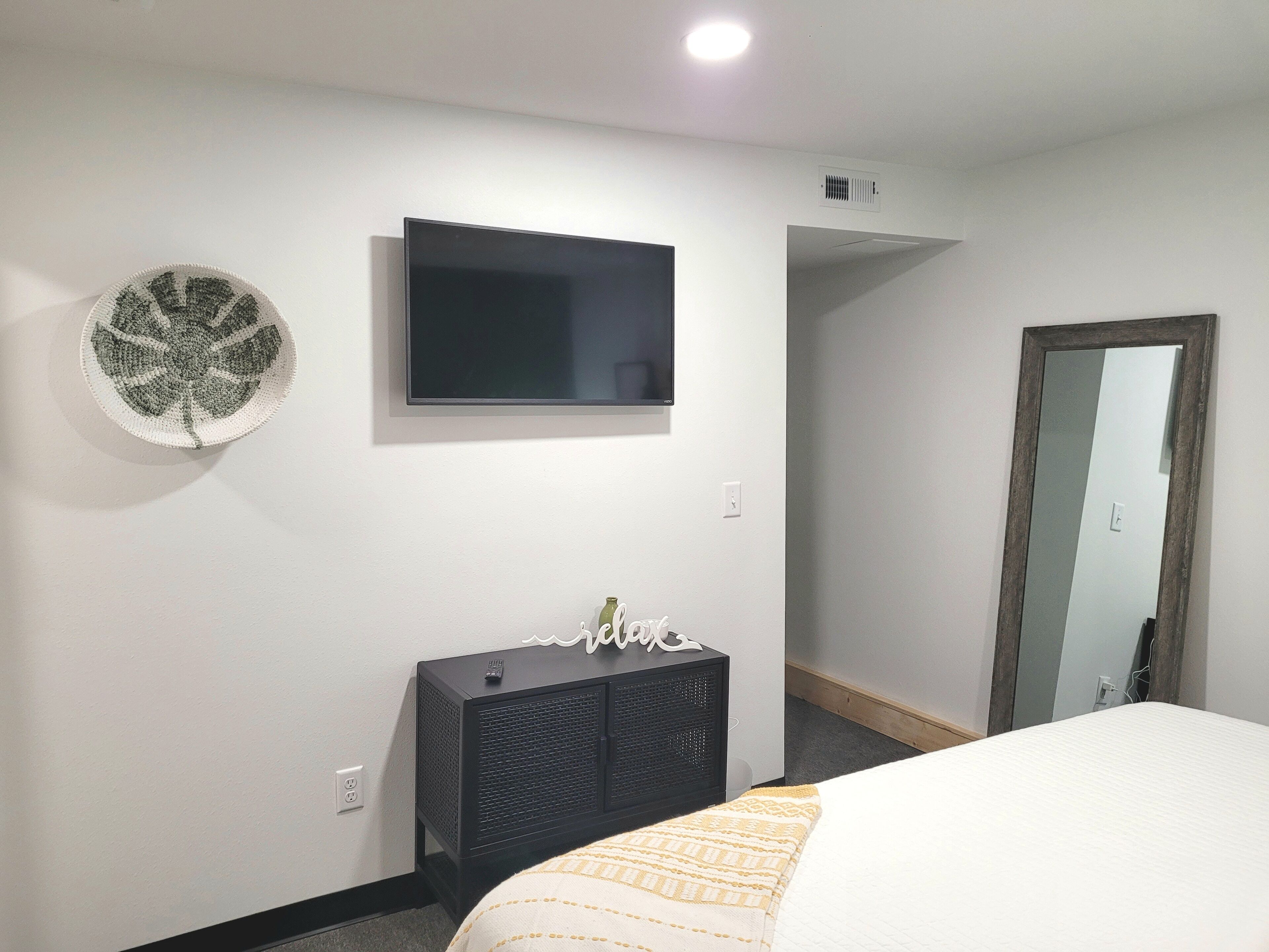A hotel room with a bed, a TV mounted on the wall, a small cabinet, and a mirror.