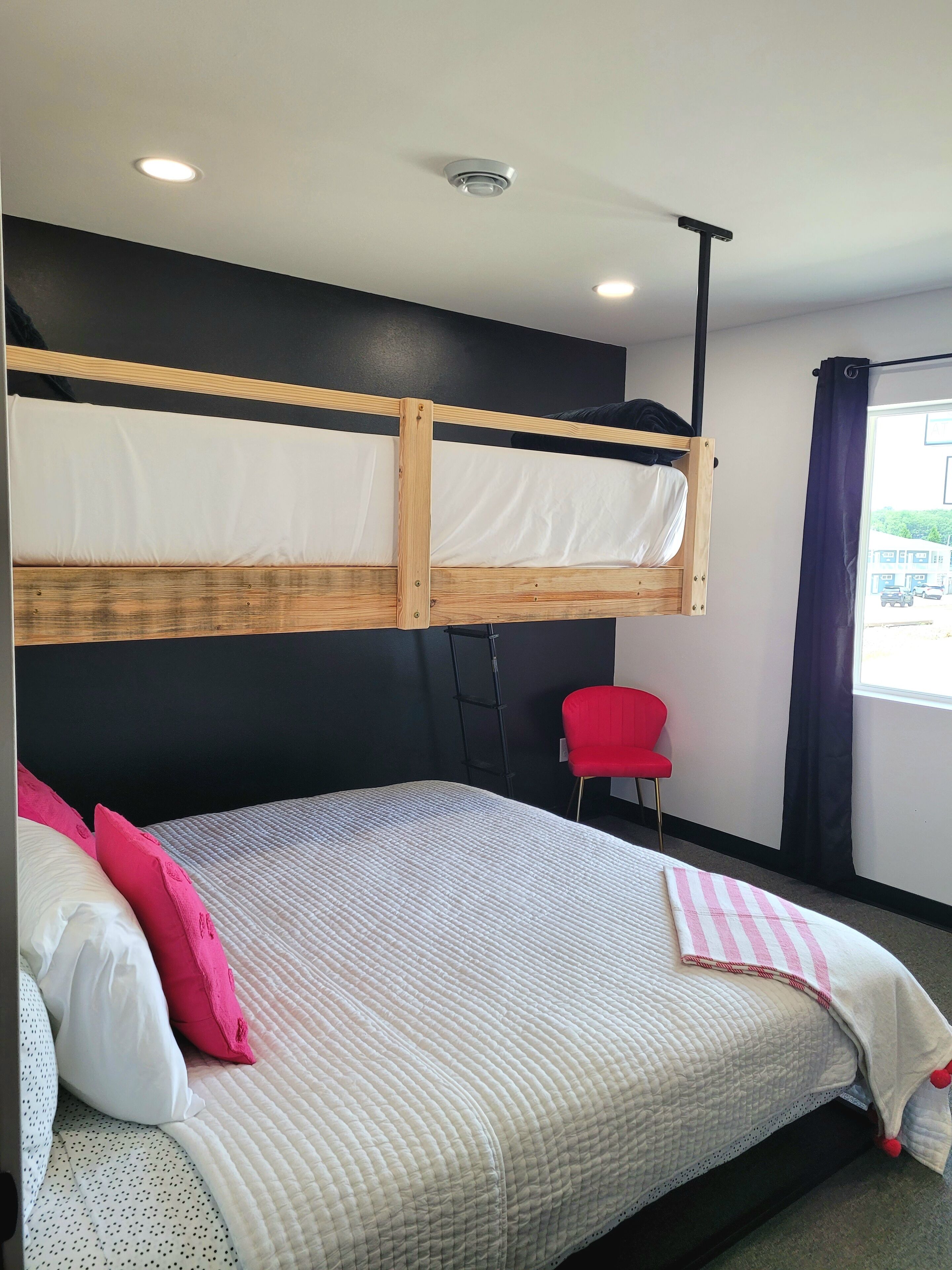 Habitació d'hotel moderna amb un llit superposat, un llit individual, una cadira vermella i una finestra amb cortines.