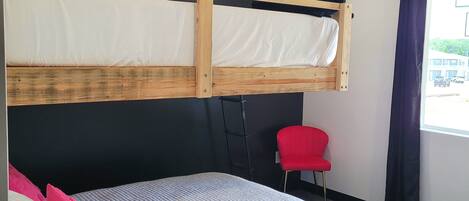Habitació d'hotel moderna amb un llit superposat, un llit individual, una cadira vermella i una finestra amb cortines.