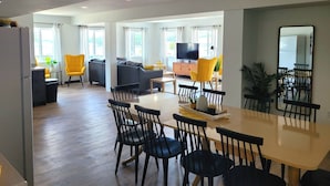 Ein modernes Wohnzimmer mit einer Couch, gelben Sesseln, einem Esstisch mit Stühlen, einem Fernseher und einem großen Spiegel.