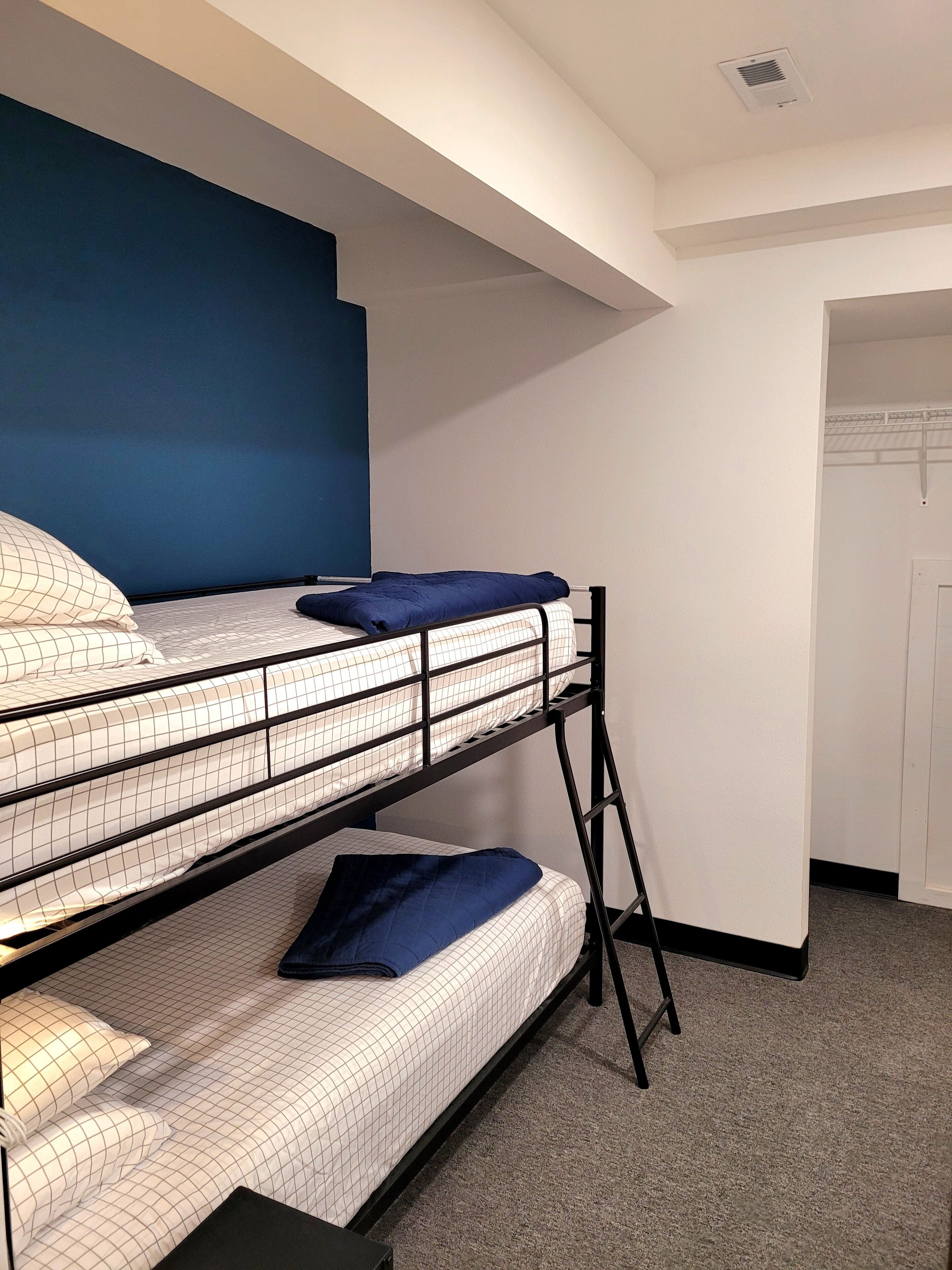 Habitación con literas, cabecera azul, ropa de cama blanca y alfombra gris.