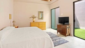 Un dormitorio con cama, cómoda de madera, televisor y puerta corrediza de vidrio que da a un balcón.