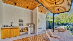 An outdoor kitchen area with a wooden deck, a grill, and a seating area with wicker furniture.