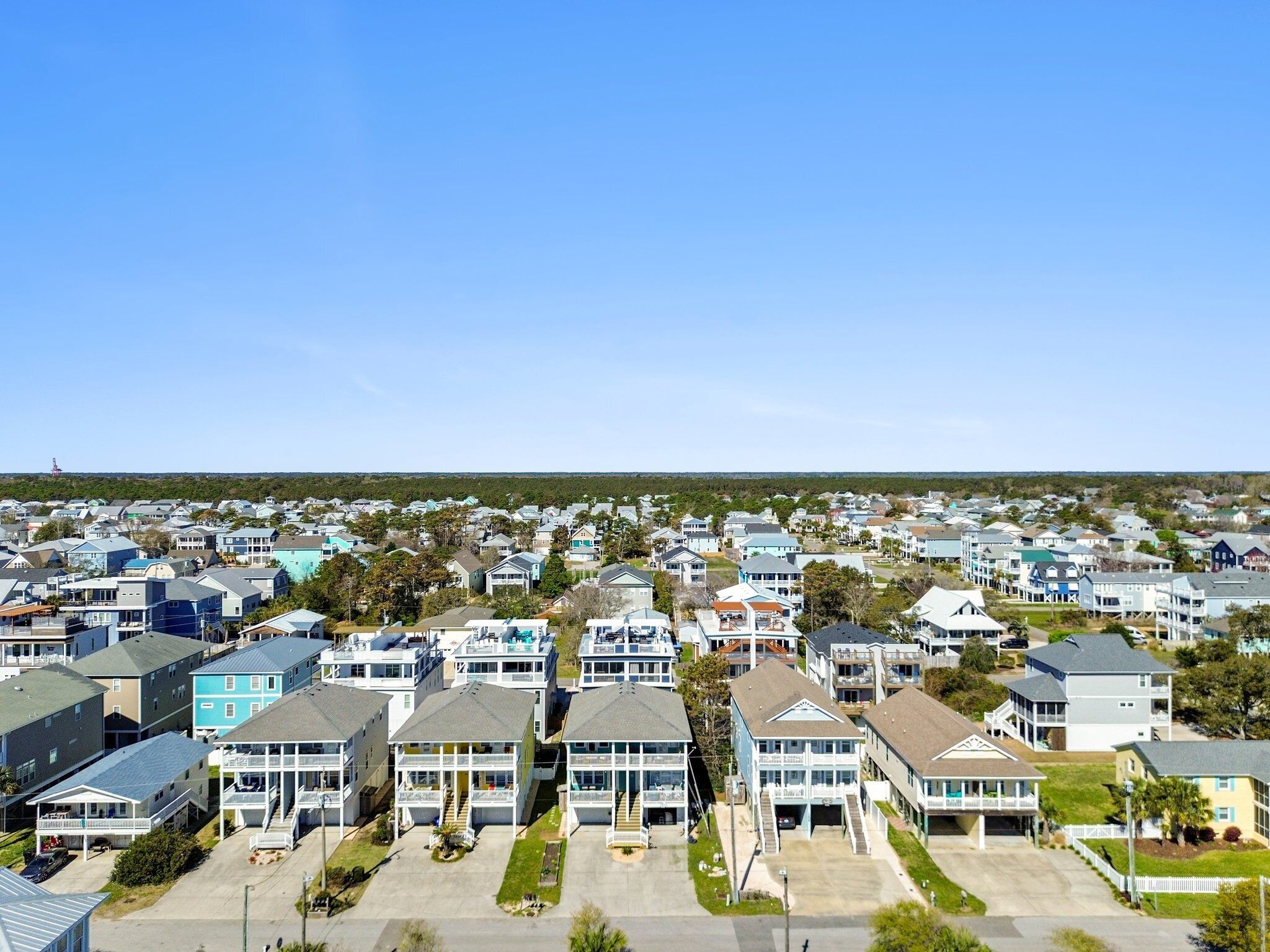 A residential area with multiple two-story houses, featuring front porches and a clear view of the ocean.