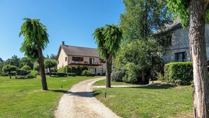 Een landhuis met een grindpad dat er naartoe leidt, omringd door groen en bomen.