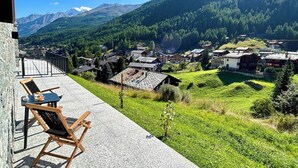 Un balcón con una silla y una mesa con vistas a un pueblo y montañas.