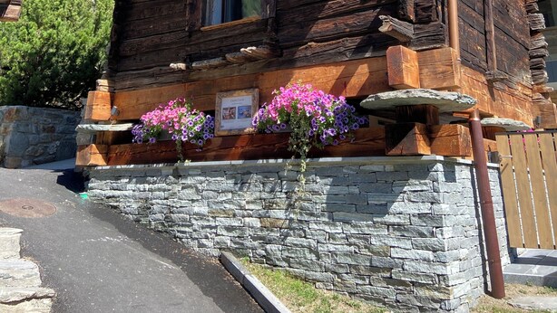 Una cabaña de troncos con base de piedra, balcón de madera y macetas con flores.