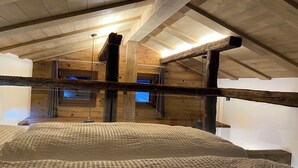 Un dormitorio en el ático con vigas de madera a la vista, una cama litera y un gran ventanal.