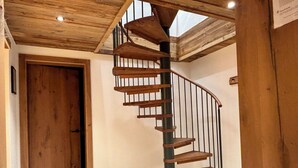 Una escalera en espiral de madera con barandilla de metal negro, que conduce a una zona superior con tragaluces.