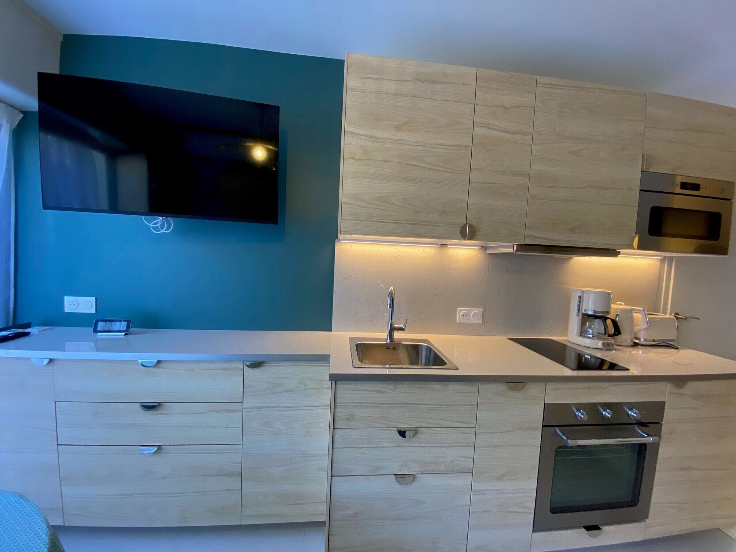 A modern kitchen with light wood cabinets, a stainless steel sink, a built-in oven, and a microwave.