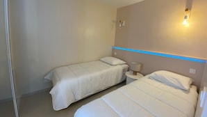 A hotel room with two beds, a nightstand, a wall-mounted lamp, and a ceiling light. - Cozy apartment with private garden near thermal baths (Balaruc-les-Bains)