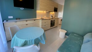 A compact kitchen with a dining area, a TV mounted on the wall, and a modern light fixture. - Cozy apartment with private garden near thermal baths (Balaruc-les-Bains)