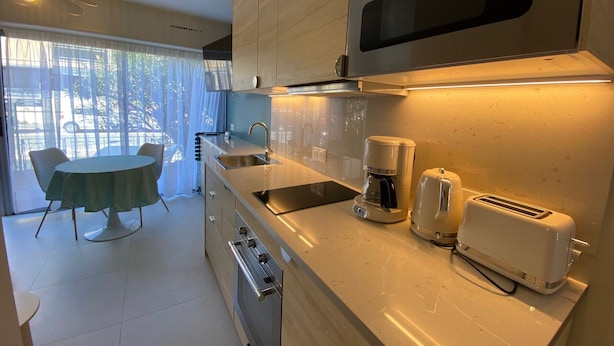 A modern kitchen with a built-in oven, a coffee maker, and a toaster. There is a dining area with a table and chairs. - Cozy apartment with private garden near thermal baths (Balaruc-les-Bains)