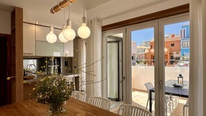 A modern kitchen with a dining area, large sliding glass doors to an outdoor patio, and a view of neighboring buildings. - Lótus by Check-in Portugal (Quarteira)