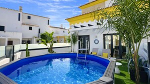 A swimming pool with a ladder, surrounded by white buildings with yellow accents, and a small garden area with plants. - Lótus by Check-in Portugal (Quarteira)