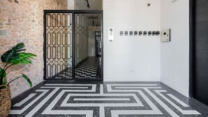 Un couloir avec un sol à carreaux, un mur en pierre, une grille en métal et une plante en pot.