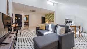 Un espace de vie moderne comprenant un canapé, une table à manger et des chaises. On aperçoit un coin cuisine au fond.