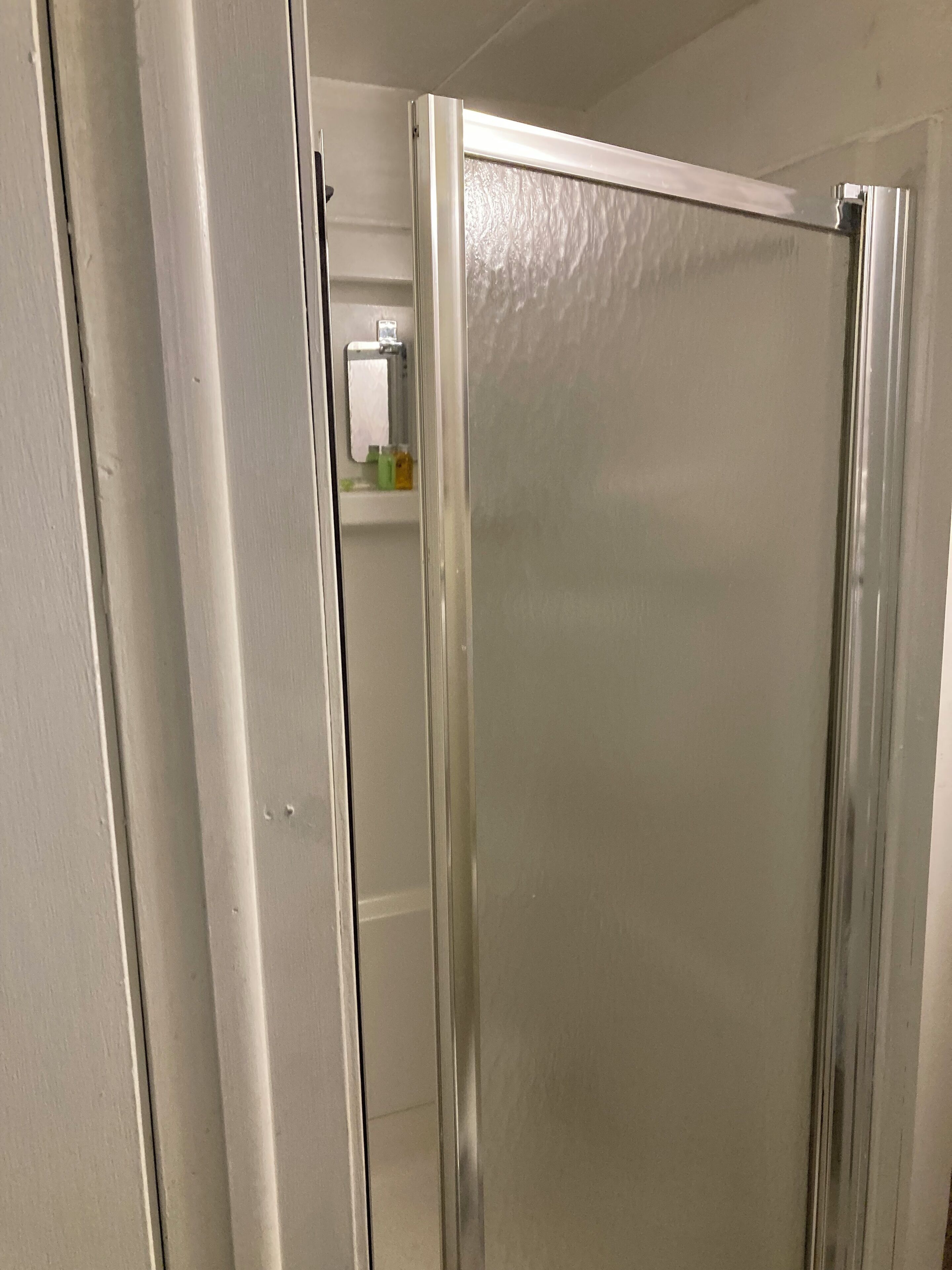 A bathroom with a white door, a mirror, and a towel dispenser.