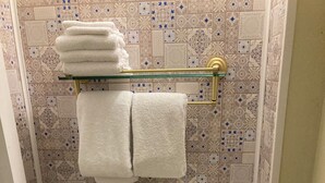 A bathroom with a toilet, a trash bin, and a towel rack with folded towels.