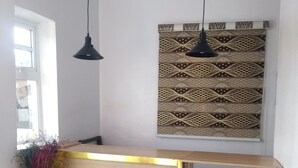 A reception desk with a wooden finish and gold trim, a woven basket vase with dried plants, and a patterned wall hanging above. - BLUE AO HOtEL (Lagos)