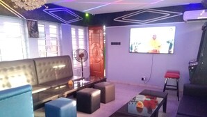 A modern living room with a sofa, ottomans, a coffee table, and a TV. - BLUE AO HOtEL (Lagos)