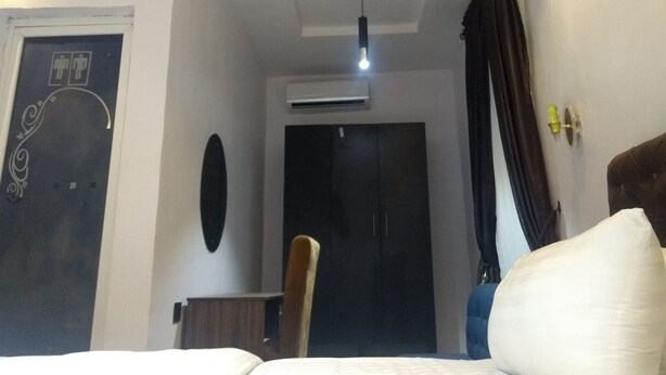 A hotel room with a bed, a chair, a door with a sign, an air conditioning unit, and a curtain. - BLUE AO HOtEL (Lagos)