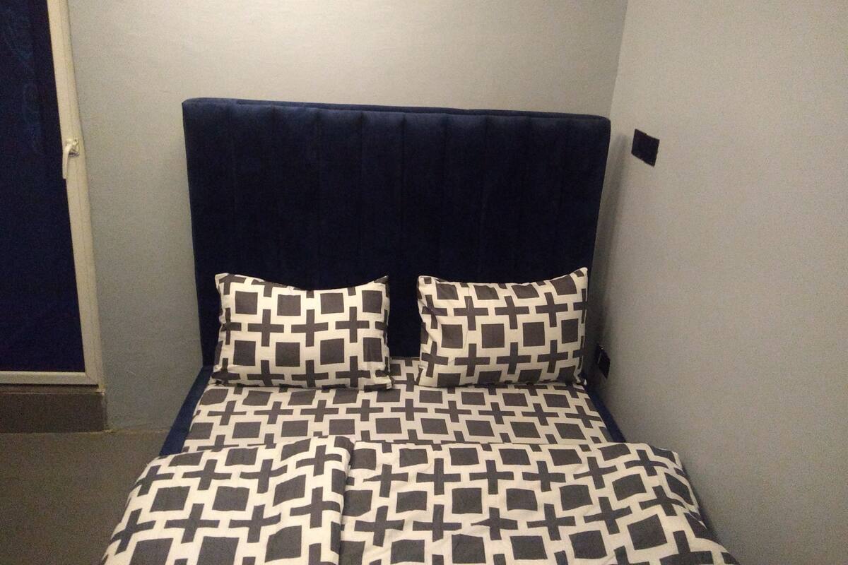 A small, neatly made bed with a dark headboard and patterned bedding.
