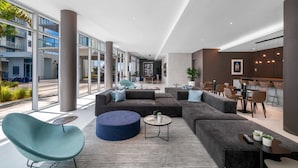 Un hall d’hôtel moderne doté d’un grand espace salon, d’un bar et de grandes fenêtres offrant une vue sur l’extérieur.