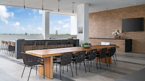 Un vaste espace extérieur aménagé pour les repas, avec une longue table en bois et des chaises noires, un mur de briques sur lequel est fixée une télévision, et une vue sur le ciel et la verdure.