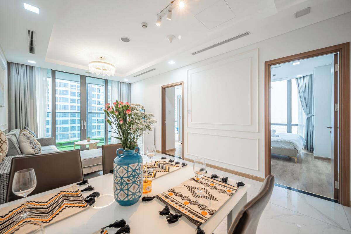 Una habitación de hotel moderna con comedor que incluye una mesa larga, sillas y un jarrón con flores.