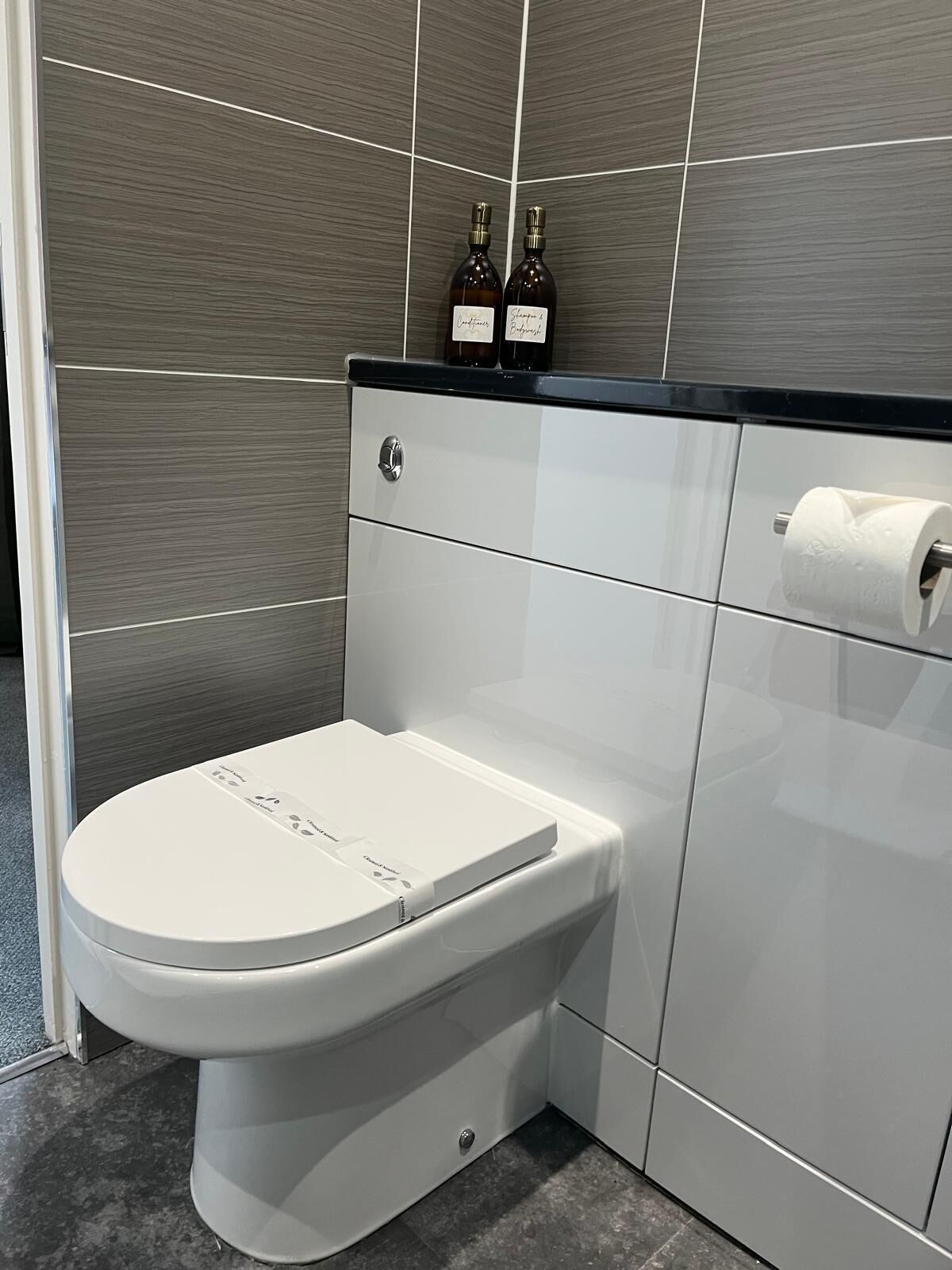 Ein modernes Badezimmer mit Toilette in Weiß, einer schwarzen Ablagefläche und zwei Seifenspendern.