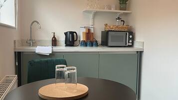 Une cuisine compacte équipée d’un four à micro-ondes, d’une bouilloire et d’une petite étagère où sont rangés de la verrerie et une plante.