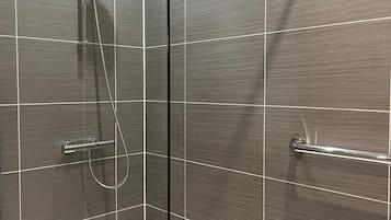 Una ducha moderna con cabezal de ducha manual y grifo empotrado en la pared, zona de ducha con mampara de vidrio y una bañera blanca.